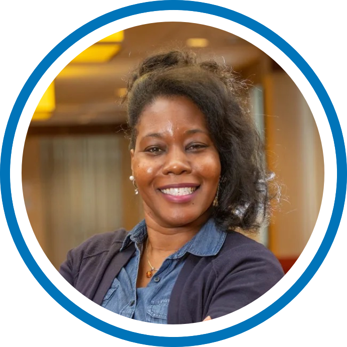 Headshot of Kwanza Yates, a woman with her hair tied up, wearing a denim shirt and a navy cardigan